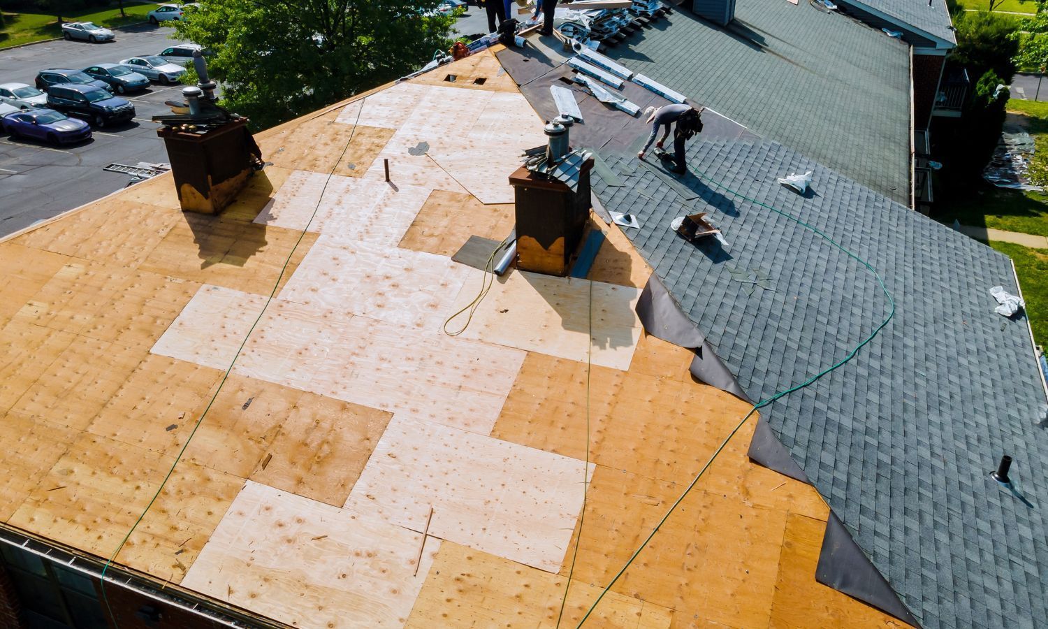 Roofers working on a residential roof, some shingles removed, plywood visible.