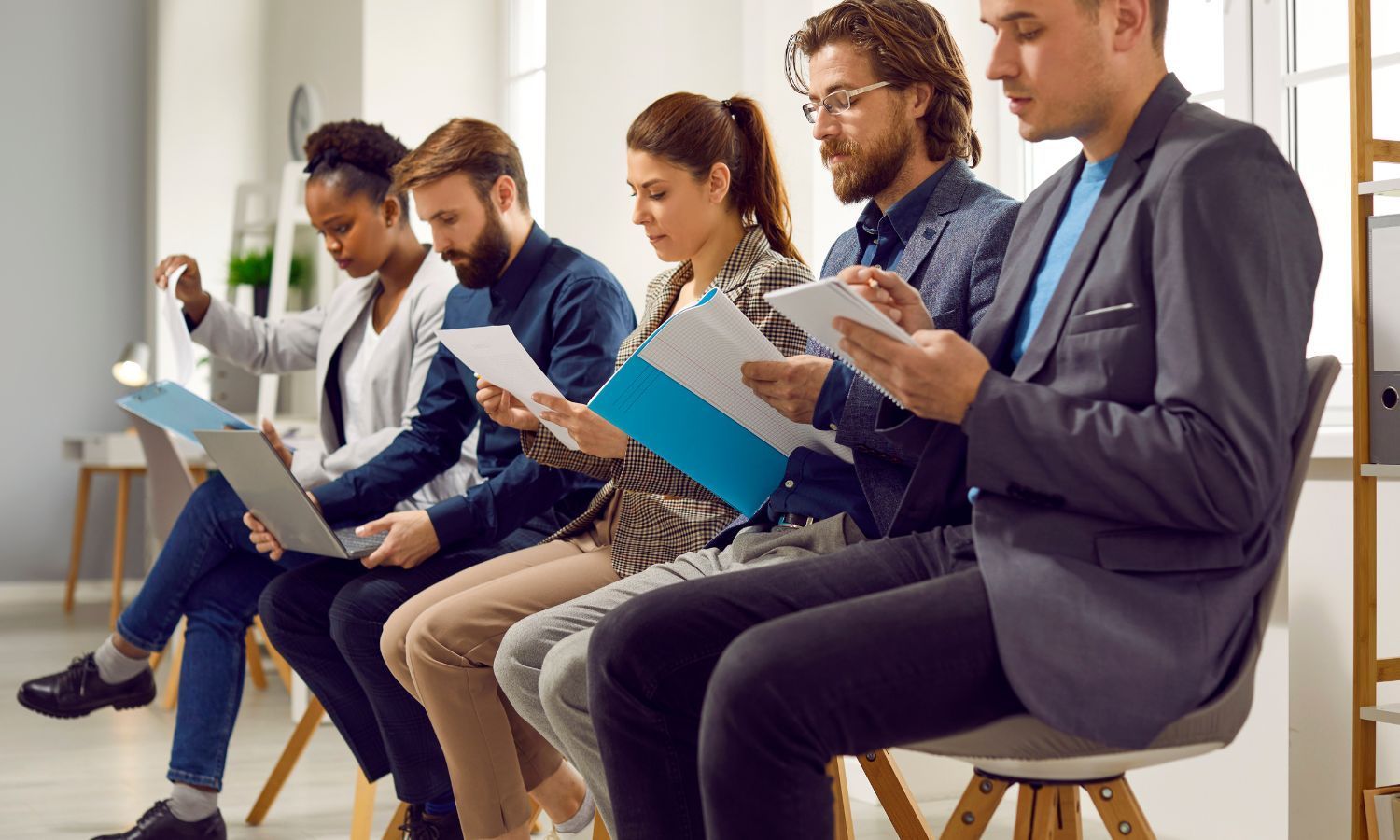 People sitting, reviewing documents or using laptops, possibly waiting for an interview.