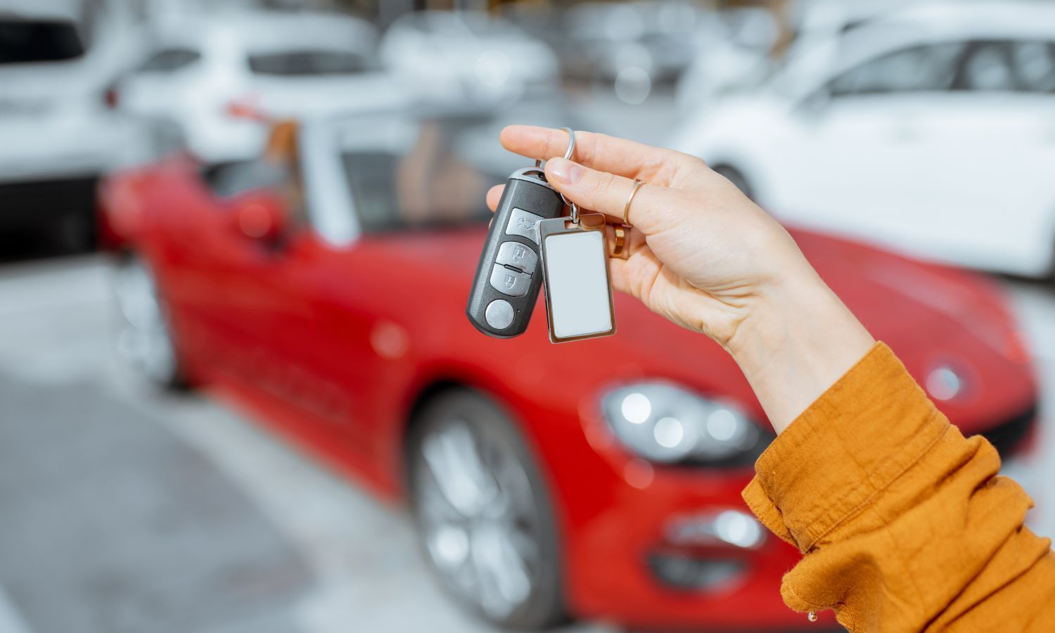 Person holding car keys in front of a red convertible.