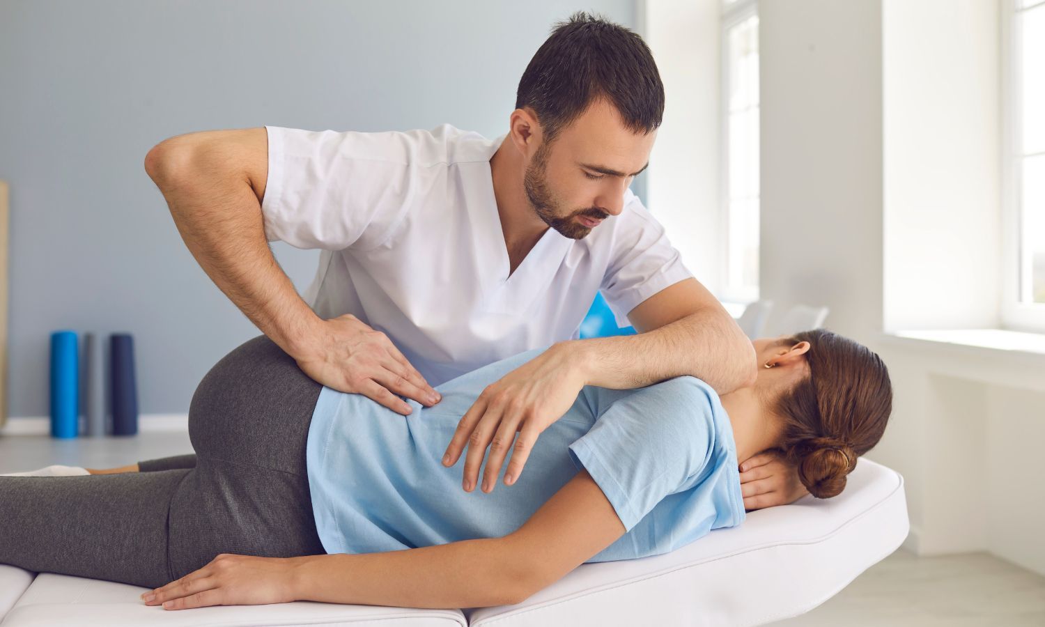 Chiropractor adjusting a woman's back on an examination table in a clinic.