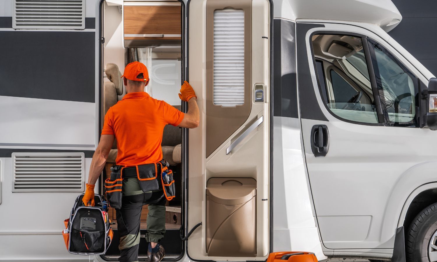 RV repair technician in orange shirt, entering RV carrying tool bag.