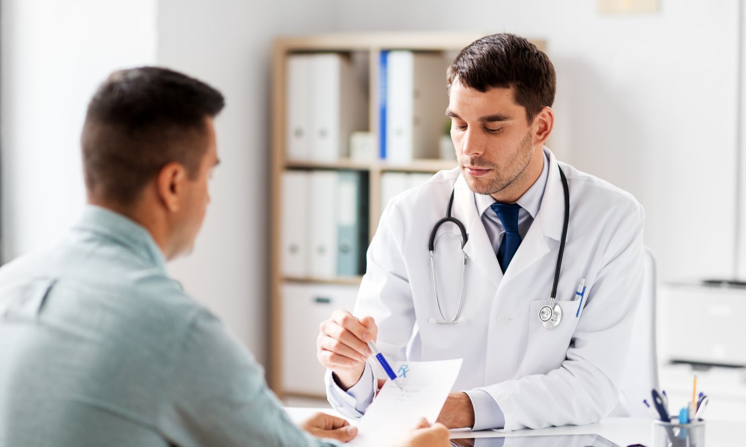 Doctor in white coat reviews paperwork with a patient in an office.