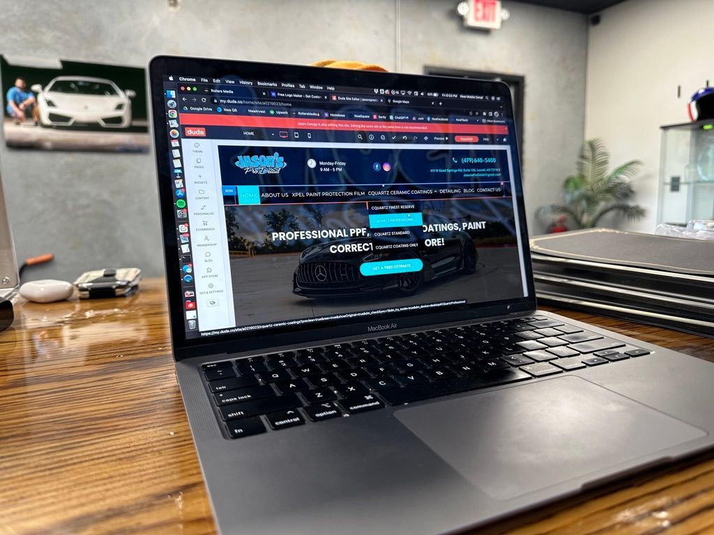 Laptop displaying a website, on a wooden desk. A car poster in the background.