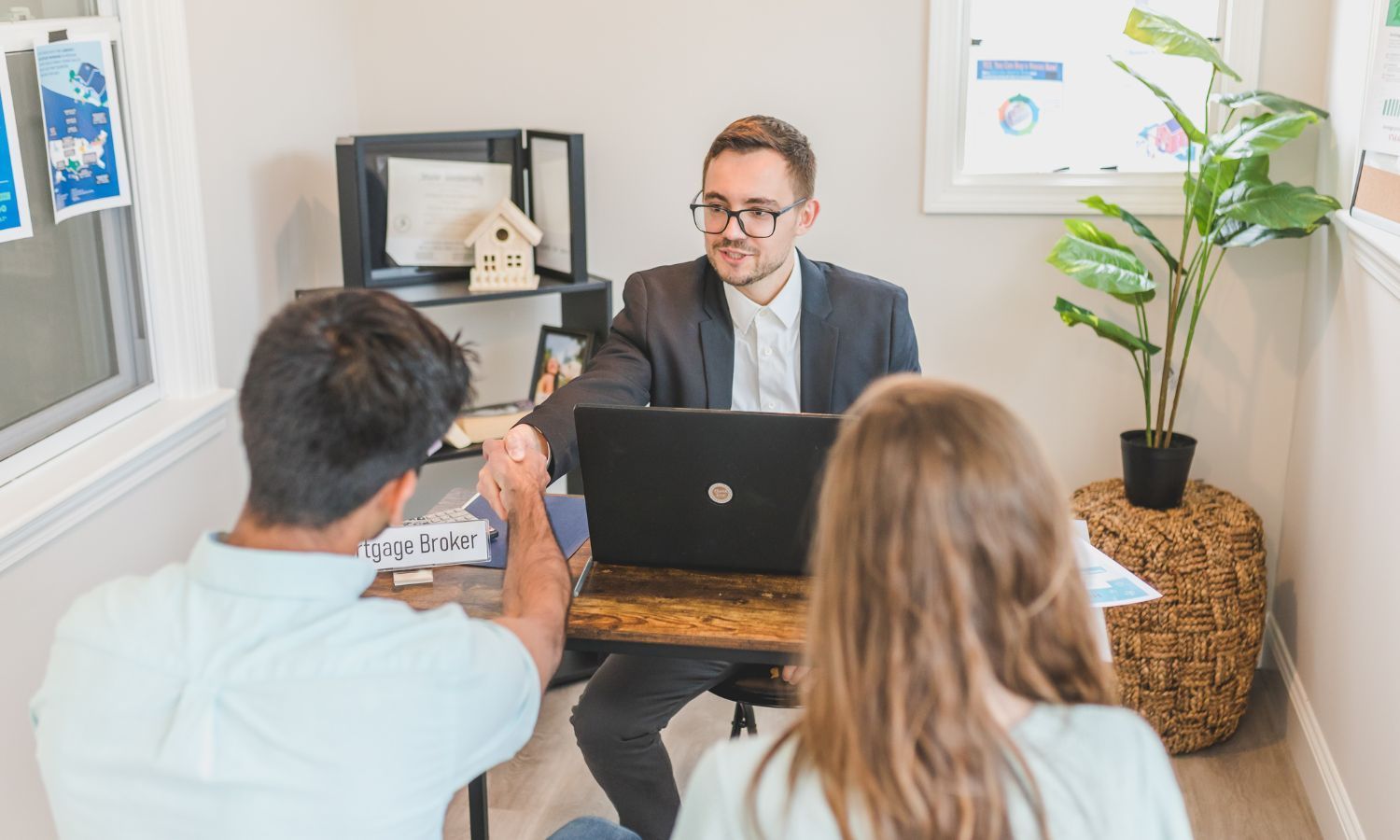 A financial advisor shaking hands with a couple at a desk with a laptop.