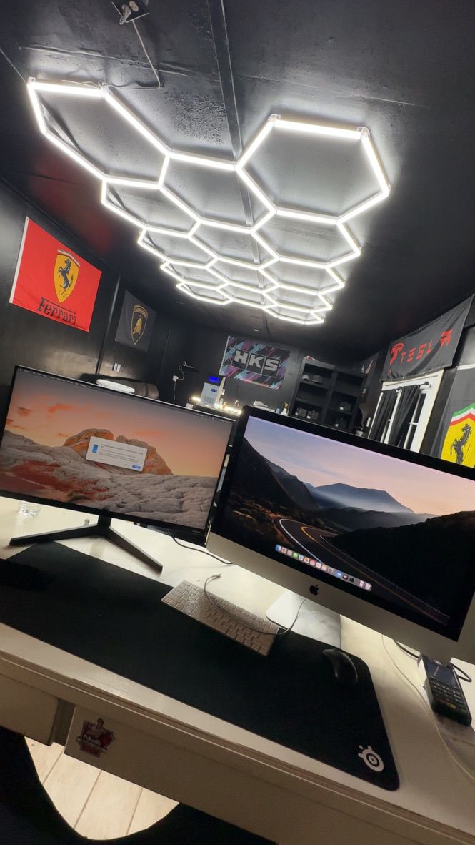 Rollers Media: Workspace with two monitors, a keyboard, and honeycomb-shaped ceiling lights. Ferrari flags are on the wall.