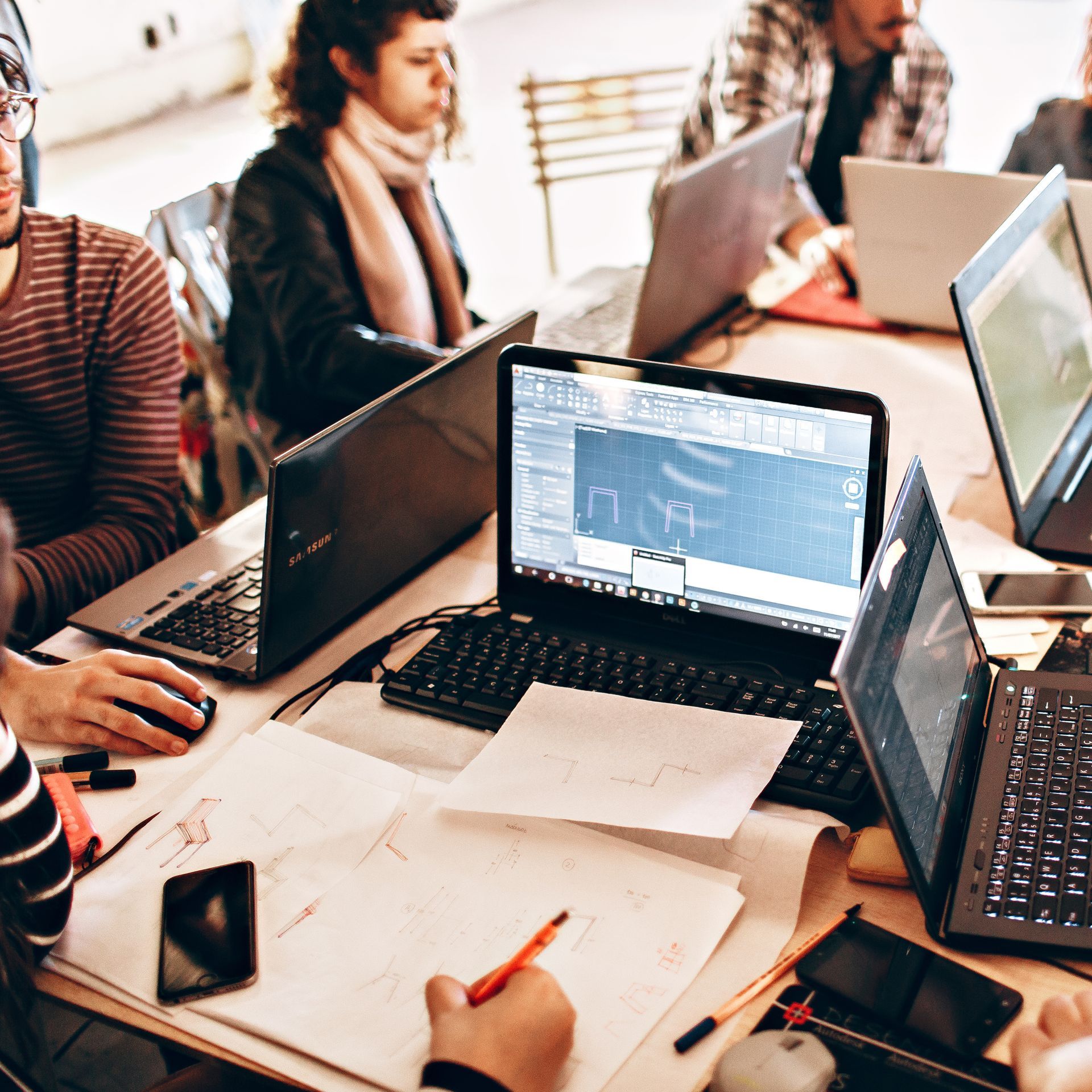 Rollers Media: People collaborating around a table with laptops, papers, and phones in a bright office setting.