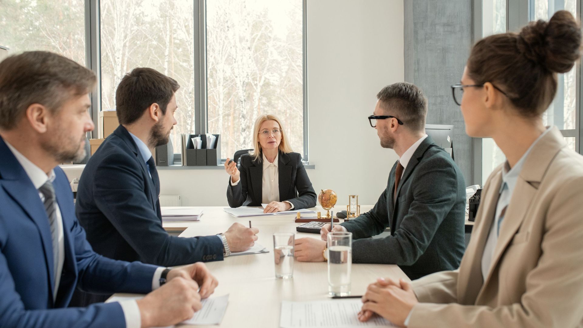 A business meeting in an office with five people sitting around a table.