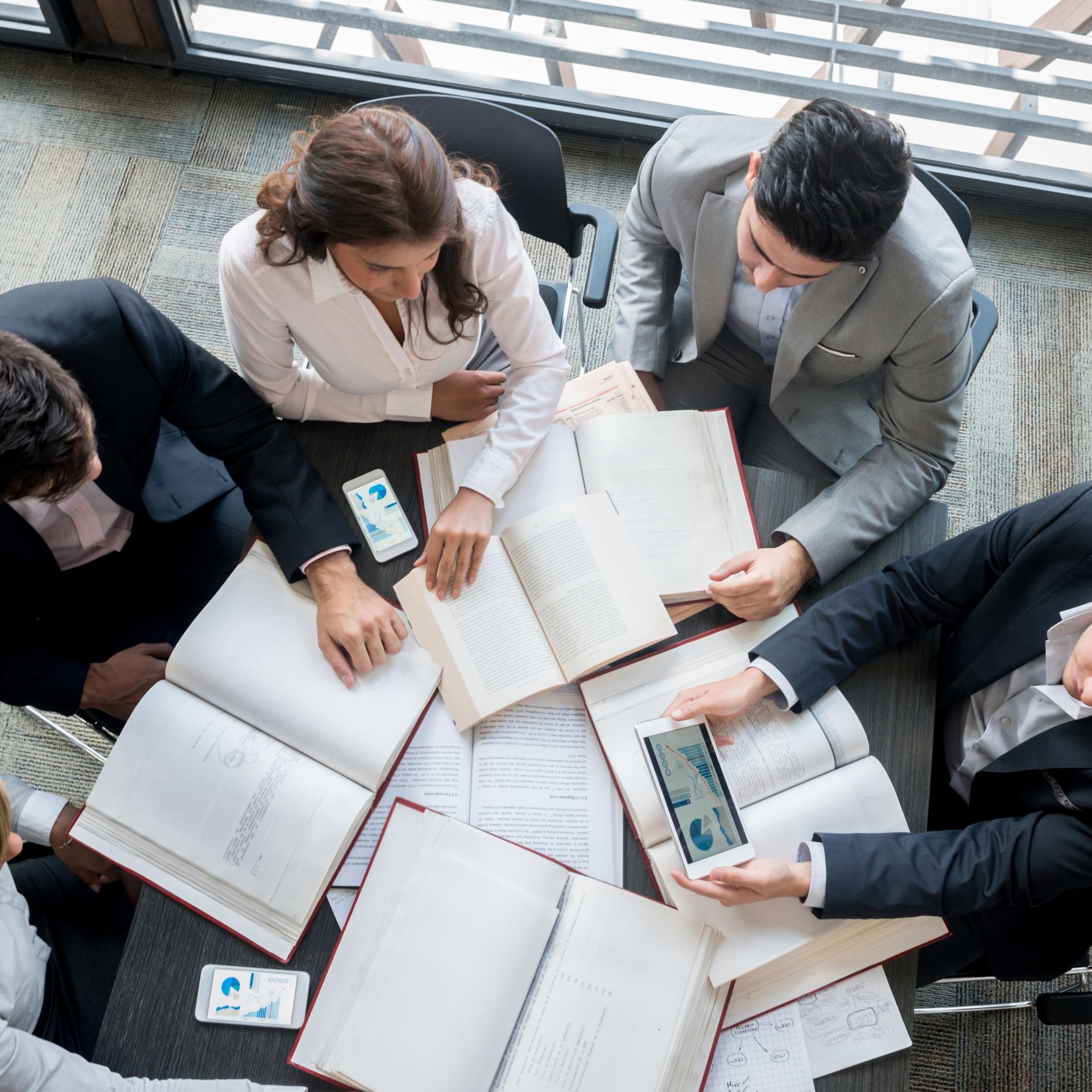 Rollers Media: Business team huddled around a table, examining open books and phones with charts, in a modern office setting.