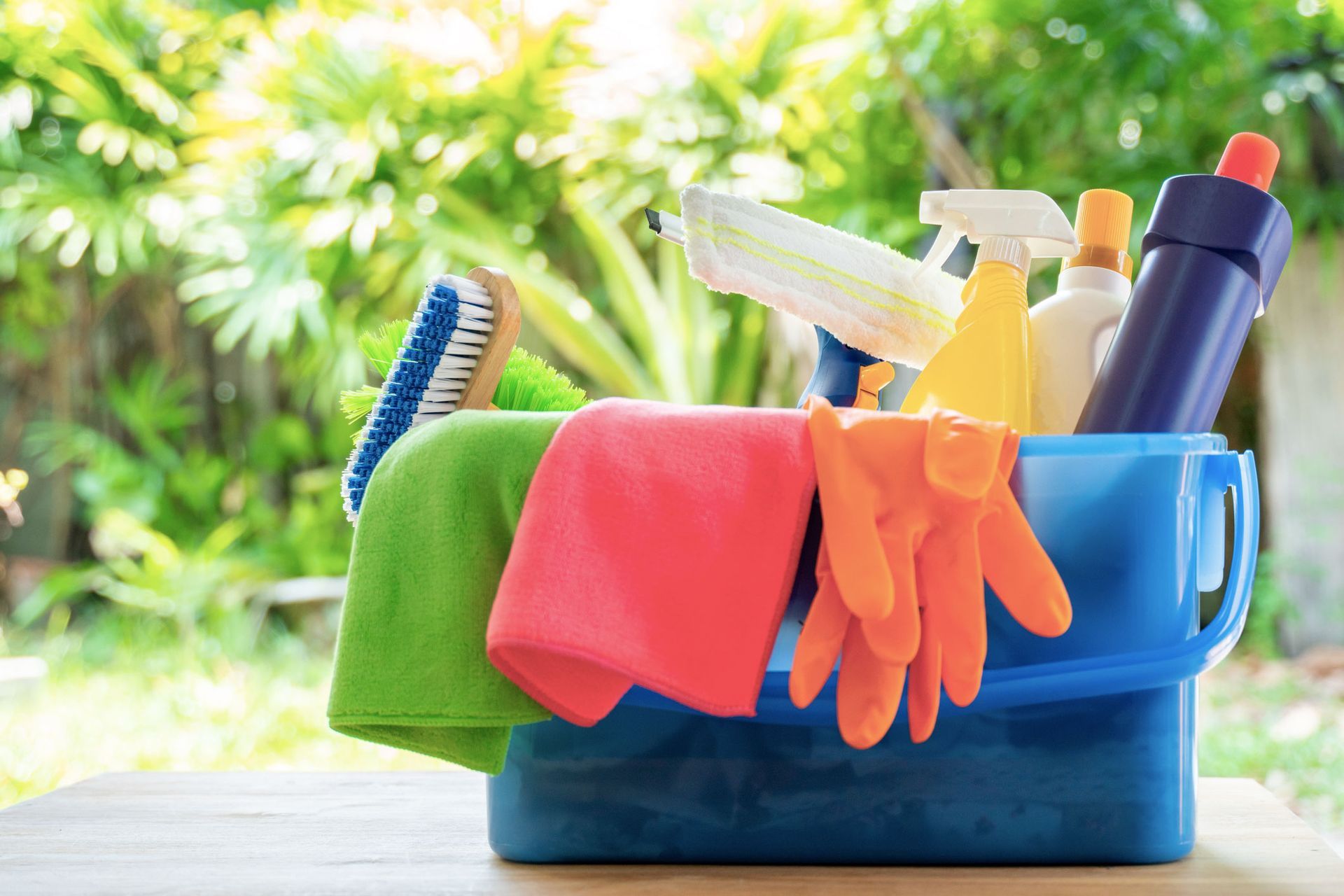 A blue bucket filled with cleaning supplies on a wooden table.