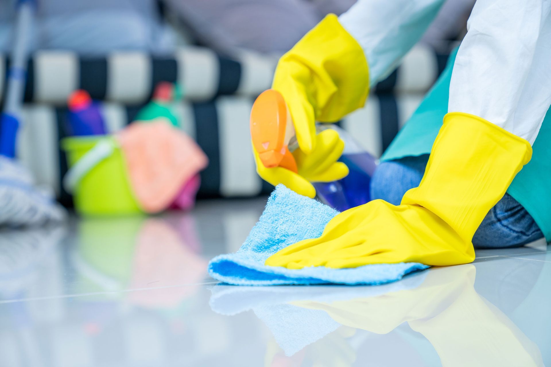A person wearing yellow gloves is cleaning the floor with a cloth and sponge.