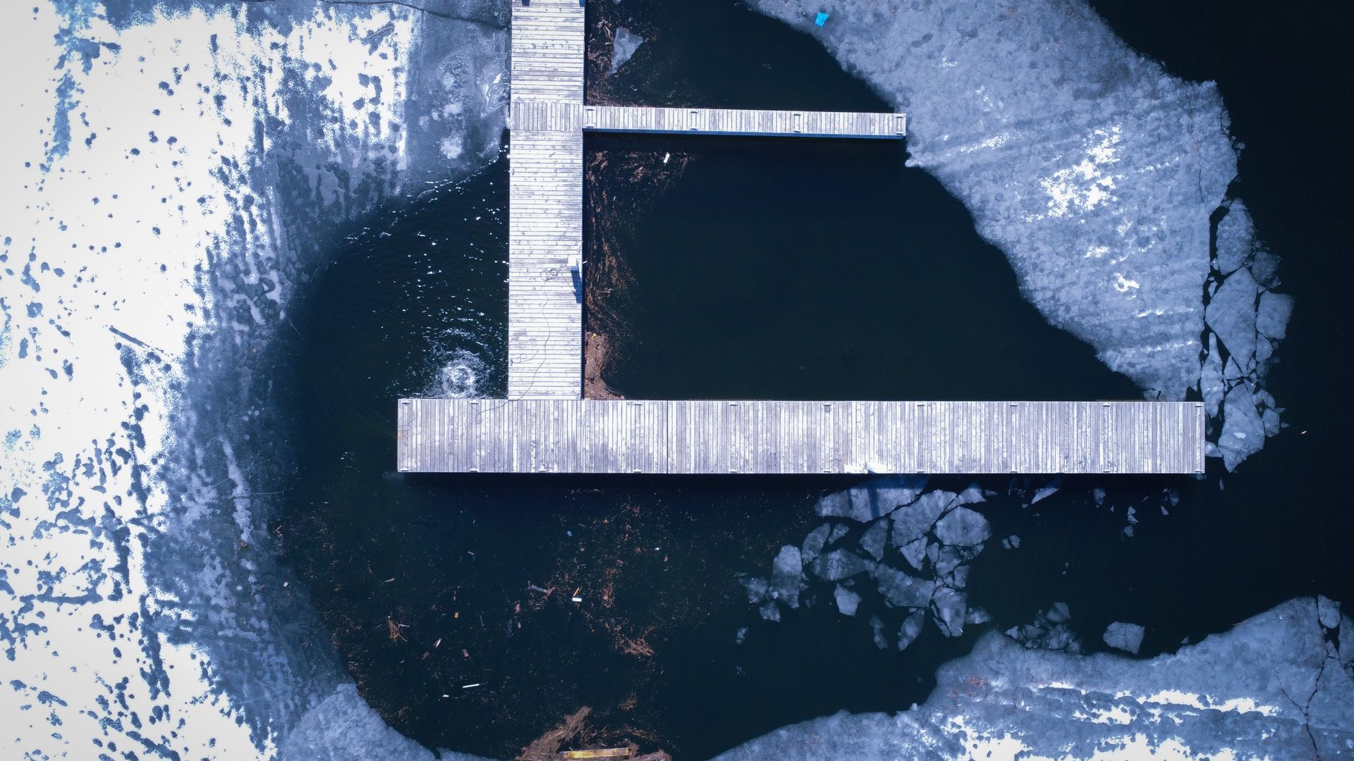 An aerial view of a dock in the middle of a lake surrounded by ice.