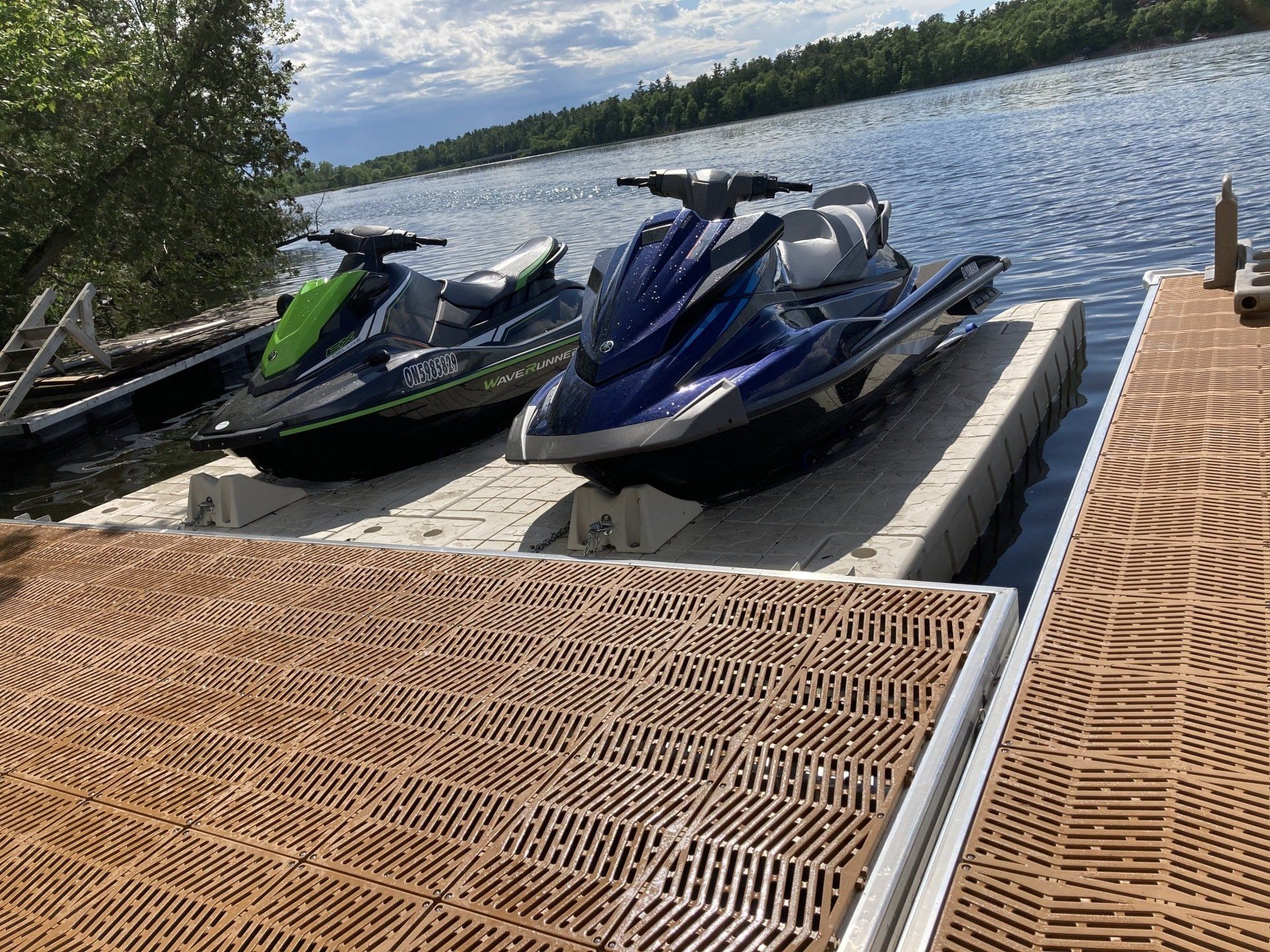 Two jet skis are parked on a dock next to a lake.