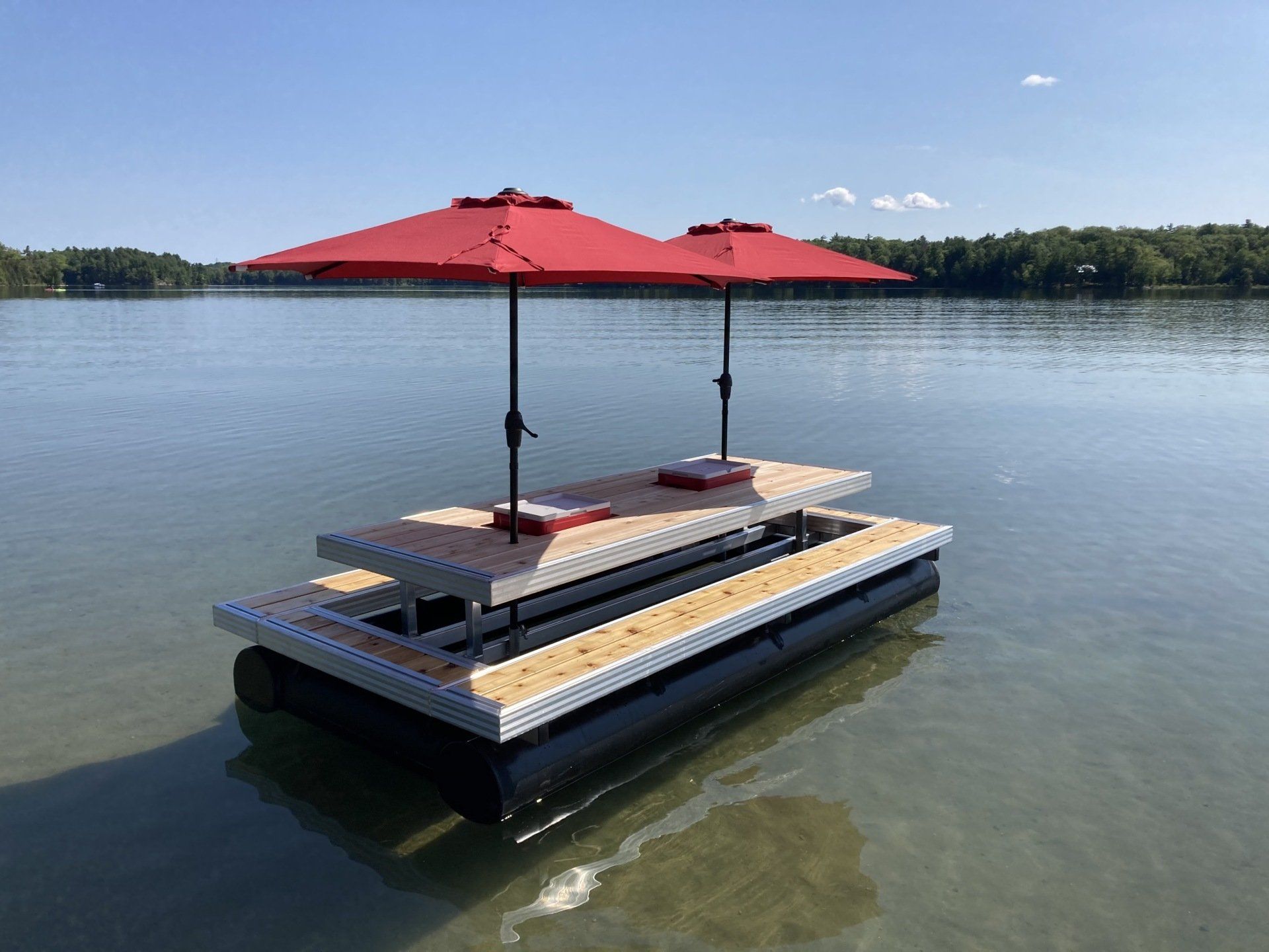 A floating picnic table with two red umbrellas on it in the water.