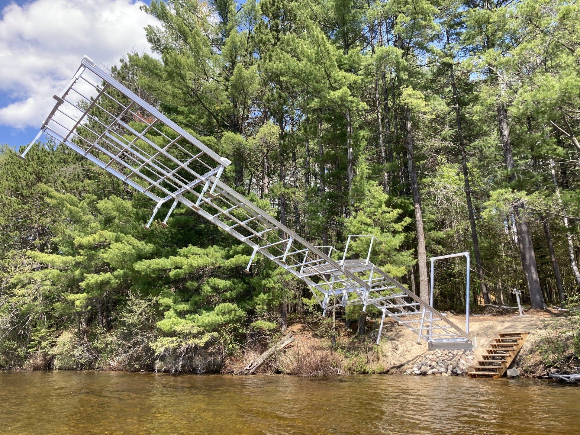A large metal structure is sitting on the shore of a lake surrounded by trees.