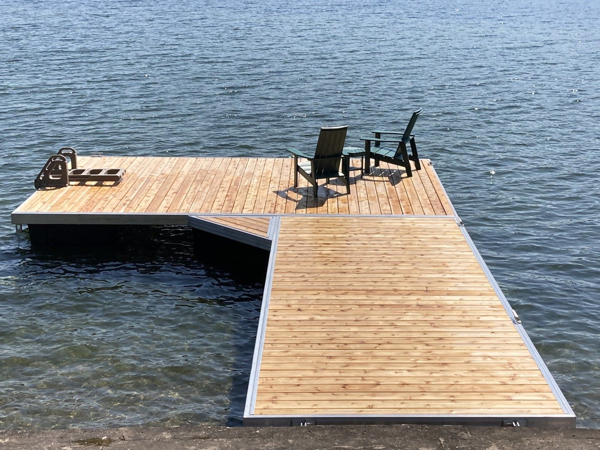 Modern floating dock extending into a calm lake with cedar decking and Adirondack chairs.