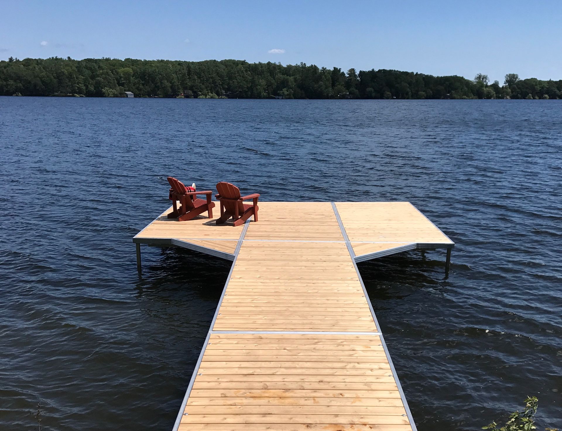 A wooden dock with two chairs on it in the middle of a lake.