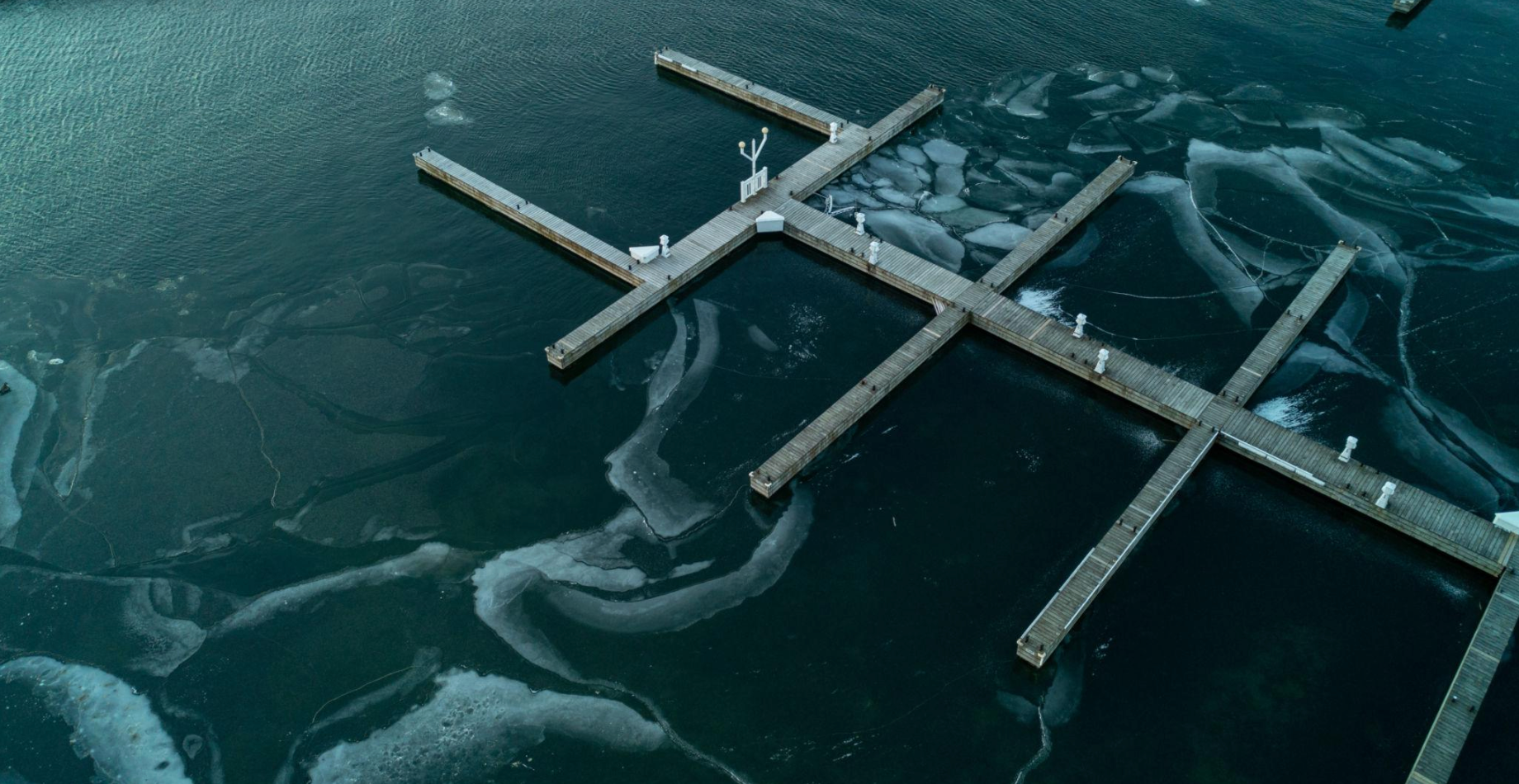Dock extending into partially frozen lake with visible ice movement patterns surrounding.