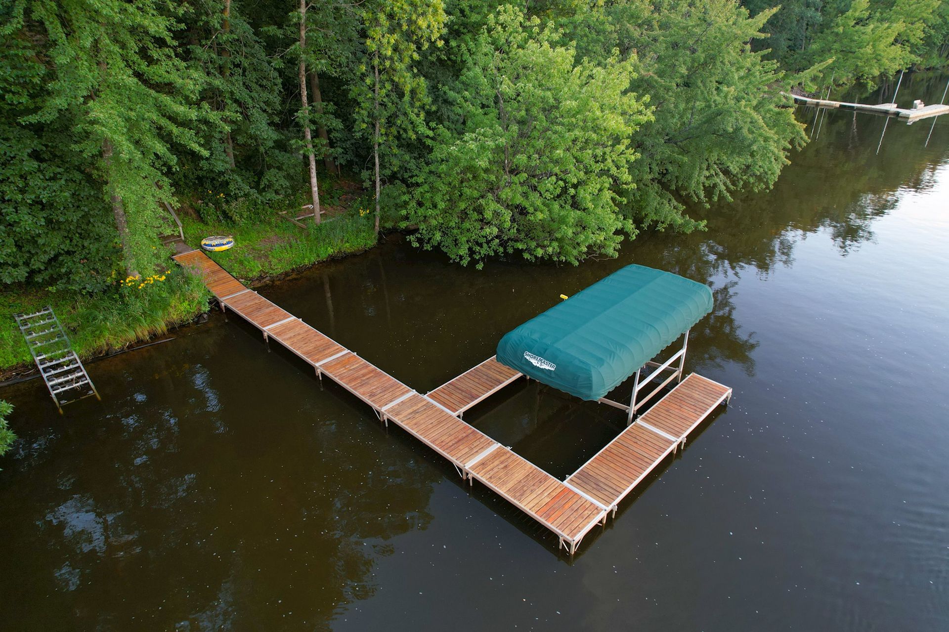 Aerial view of a floating dock system with covered boat lift extending from a wooded shoreline into 