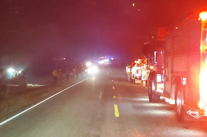 A group of fire trucks are parked on the side of a highway at night.