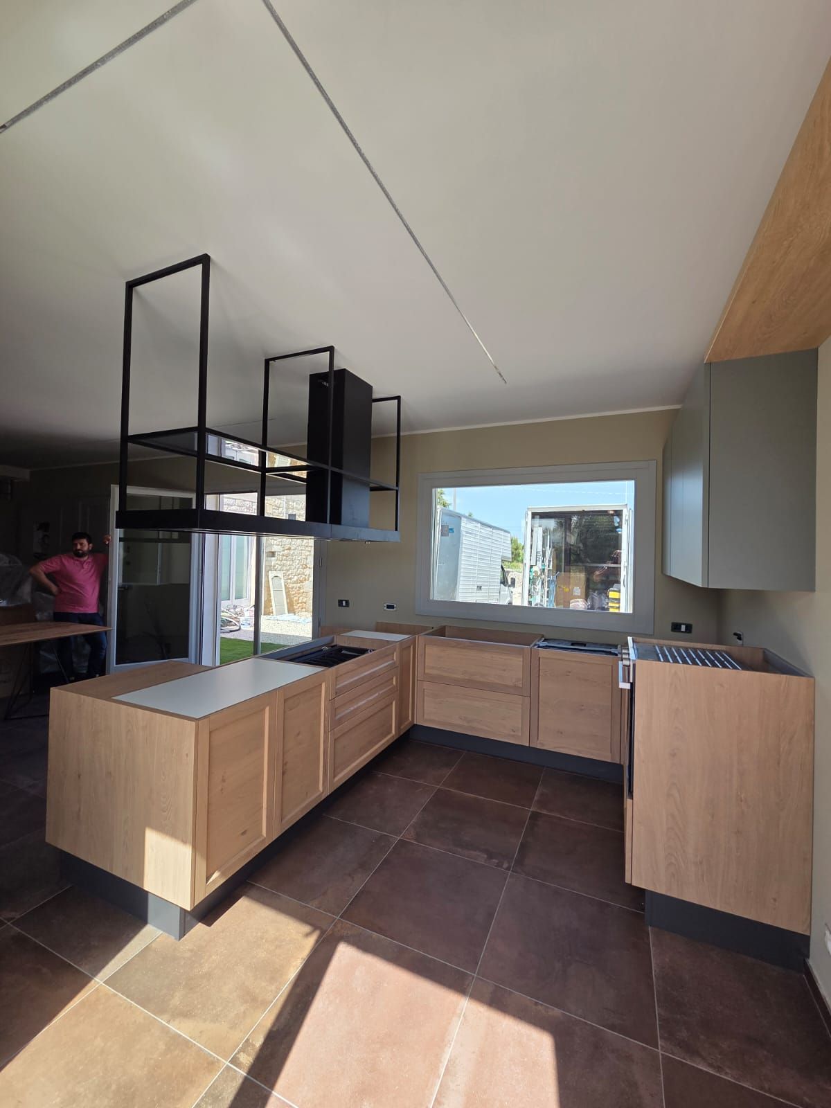 Cucina moderna in costruzione con mobili in legno, pavimento in pietra e cappa in metallo.