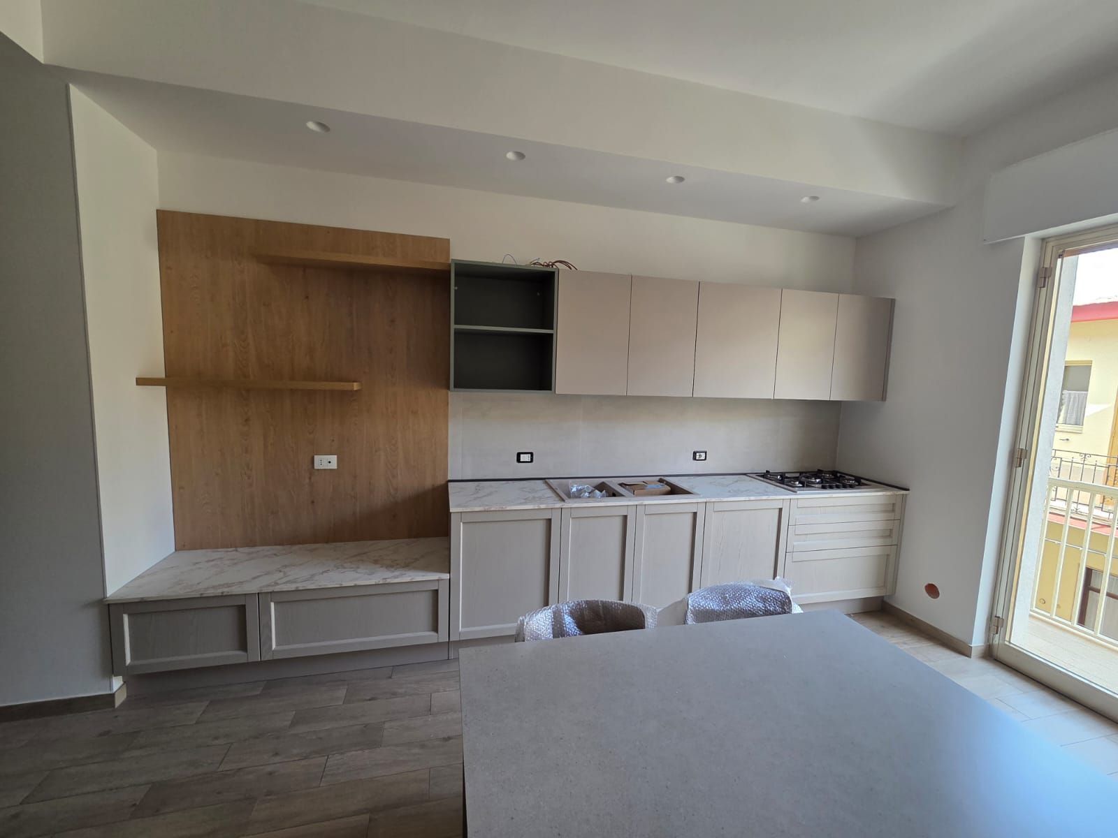 Cucina con mobili in legno chiaro, piano di lavoro e parete decorativa in legno.