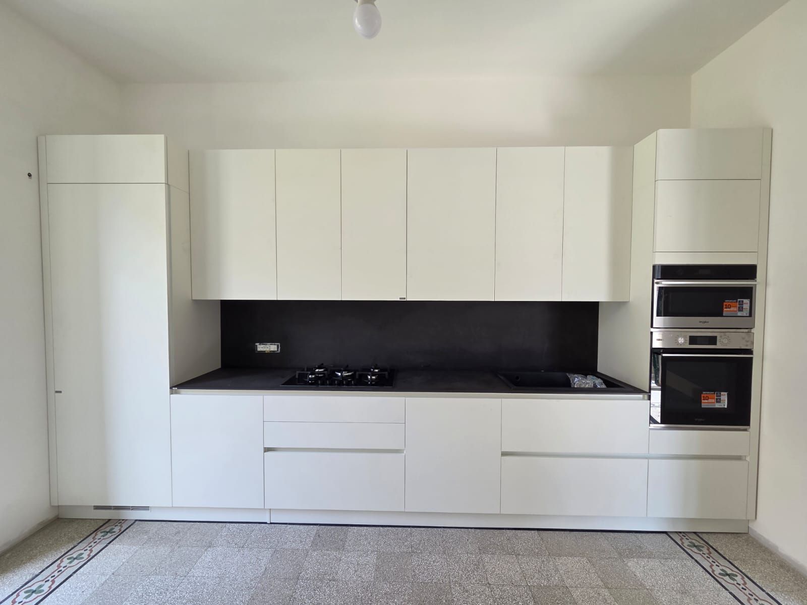 Cucina moderna bianca con piano di lavoro nero, fornelli e forni integrati.