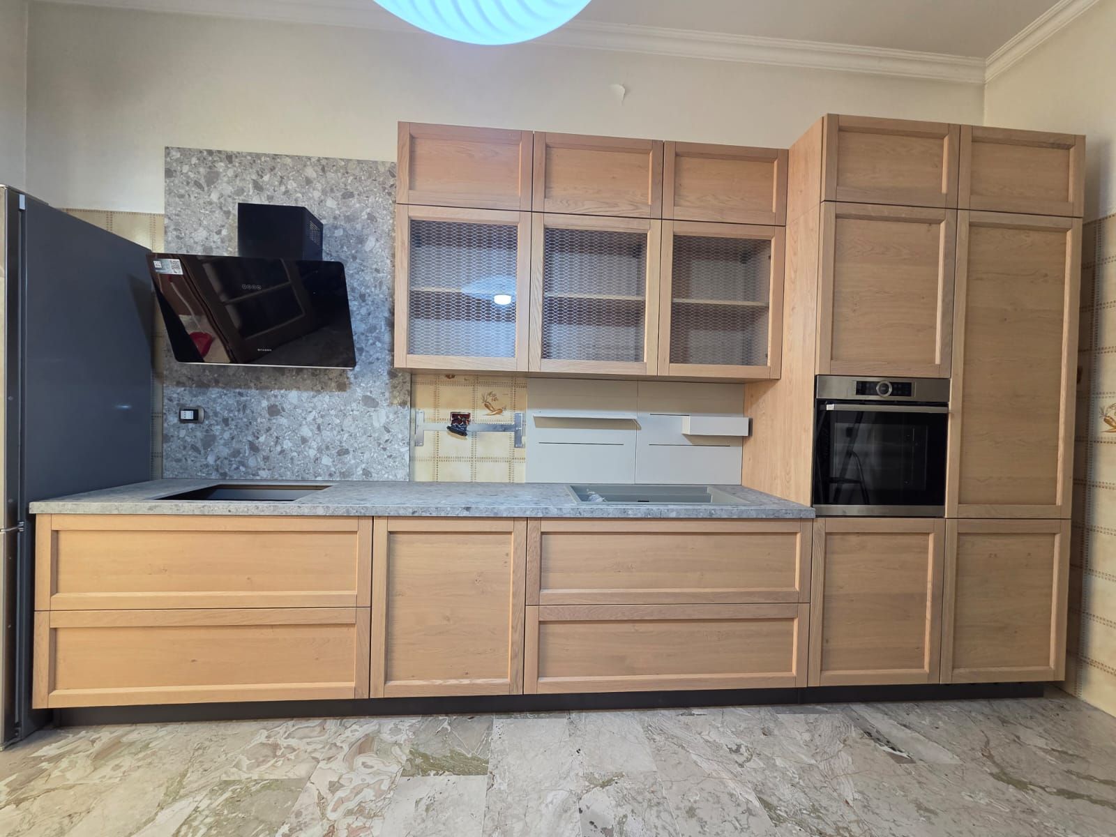 Mobili da cucina in legno chiaro con piano di lavoro grigio, forno e piano cottura neri.