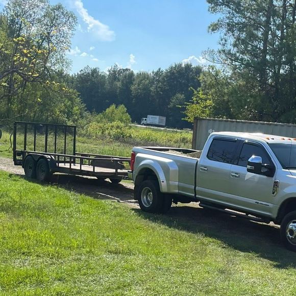A silver truck is towing a trailer in a grassy field.