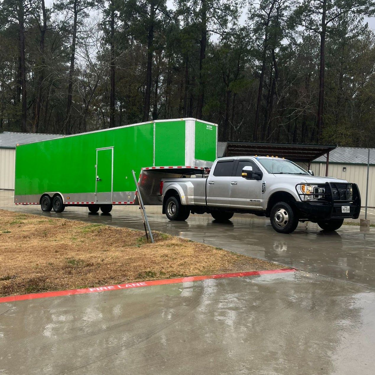 A silver truck is pulling a green trailer in a parking lot.