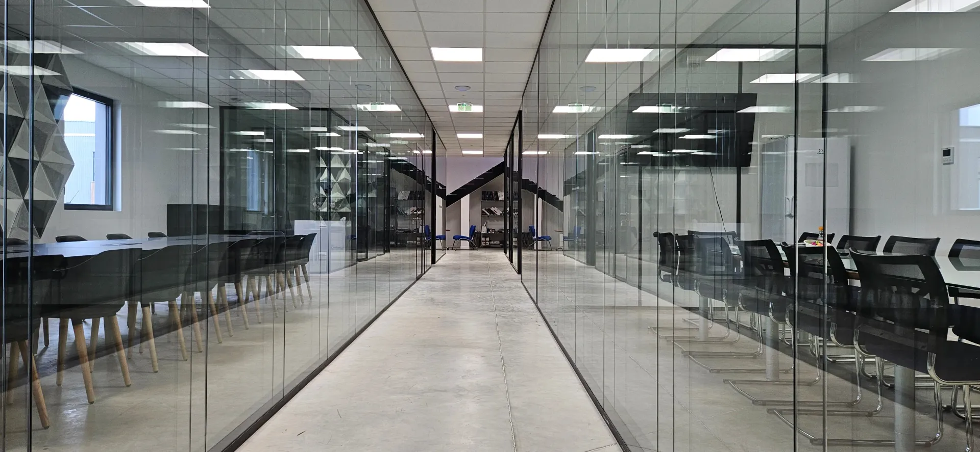 Un long couloir dans un immeuble de bureaux avec des murs en verre, des tables et des chaises. SPAC