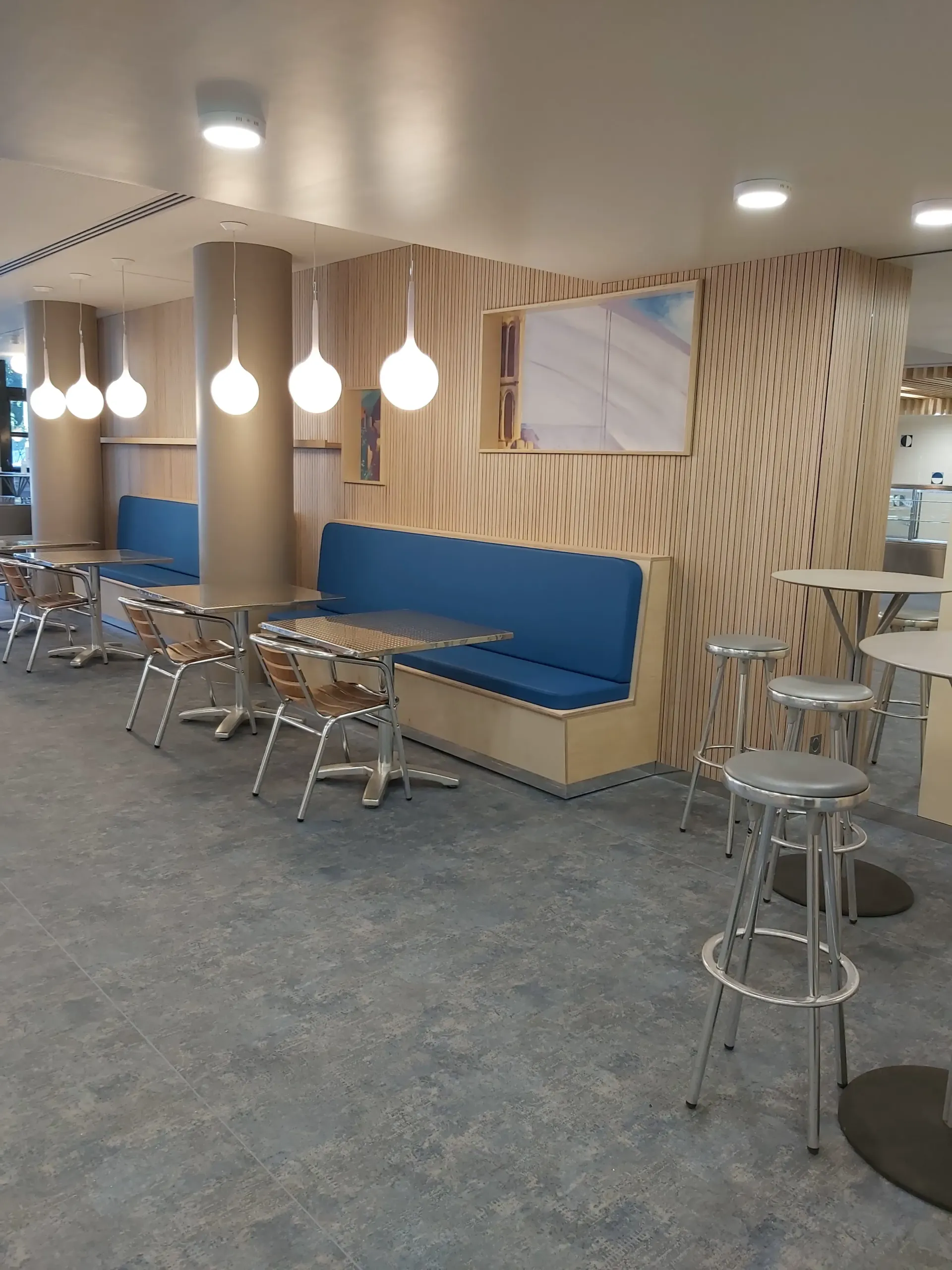 Une salle à manger avec tables et chaises et un banc bleu. Aménagement de bureaux et locaux professionnels - SPAC