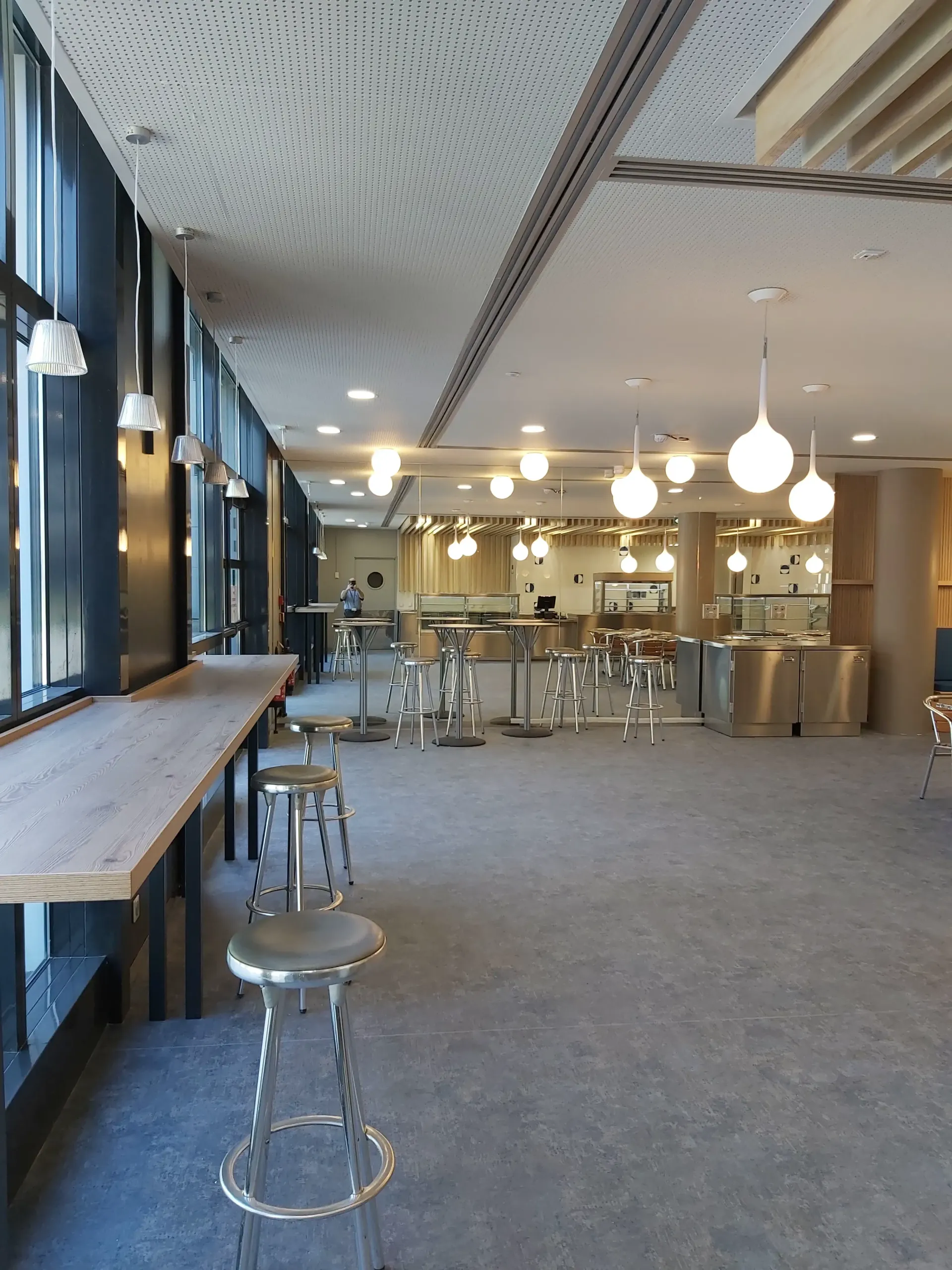 Une grande pièce avec des tables et des tabourets. Aménagement de bureaux et locaux professionnels - SPAC