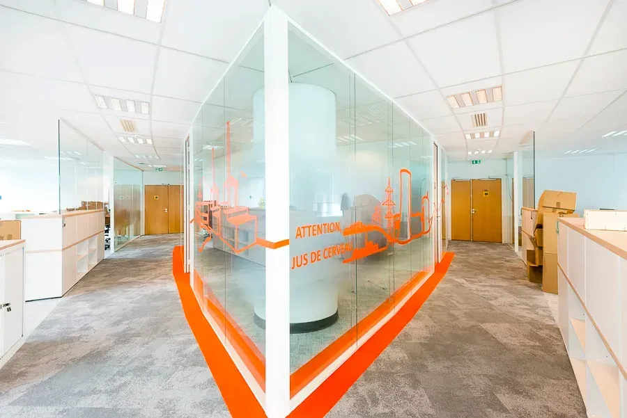 Un couloir dans un immeuble de bureaux avec un mur de verre entre deux cabines. SPAC