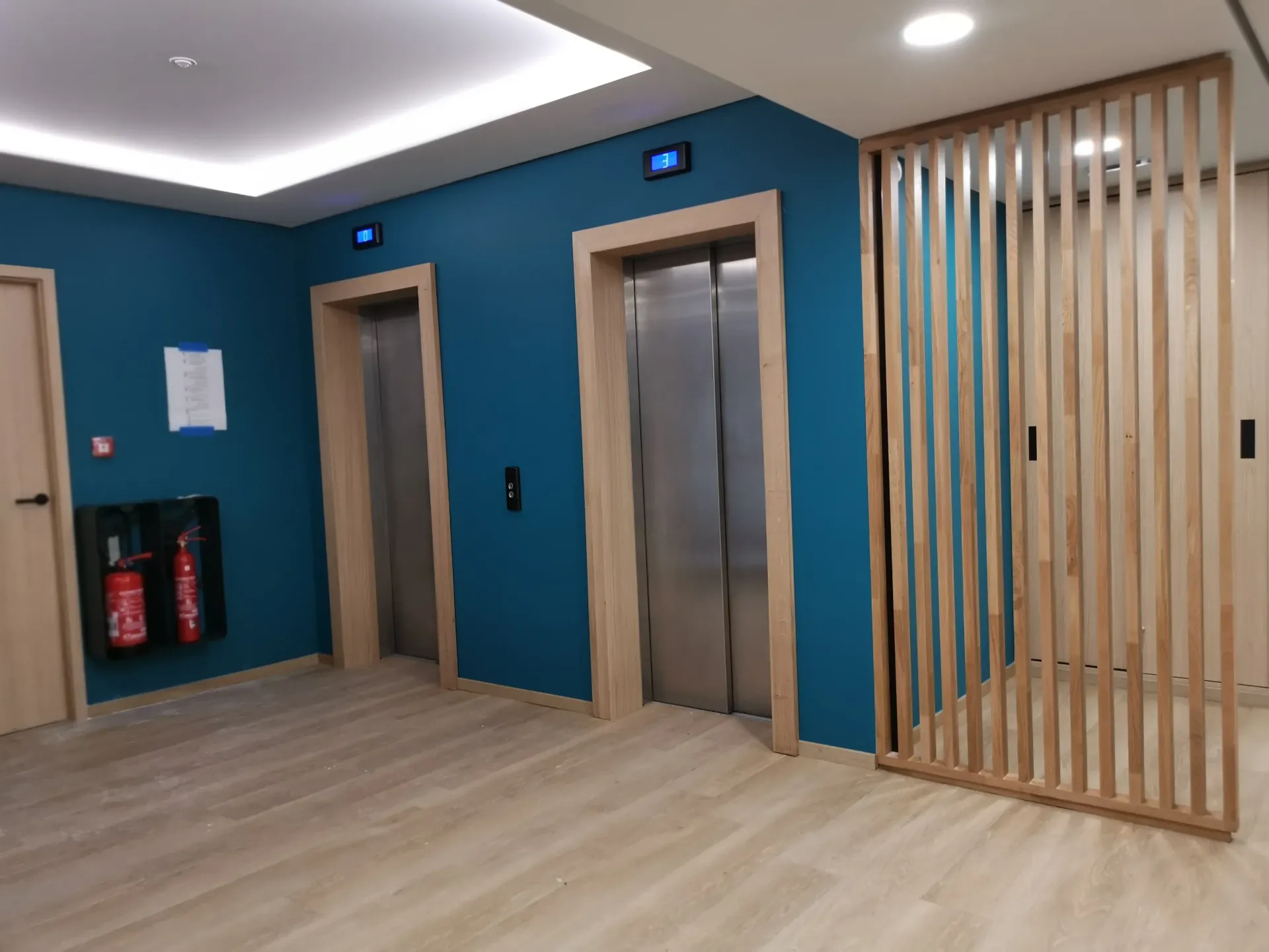 Un couloir avec deux ascenseurs et un extincteur sur le mur. Aménagement de bureaux et locaux professionnels - SPAC
