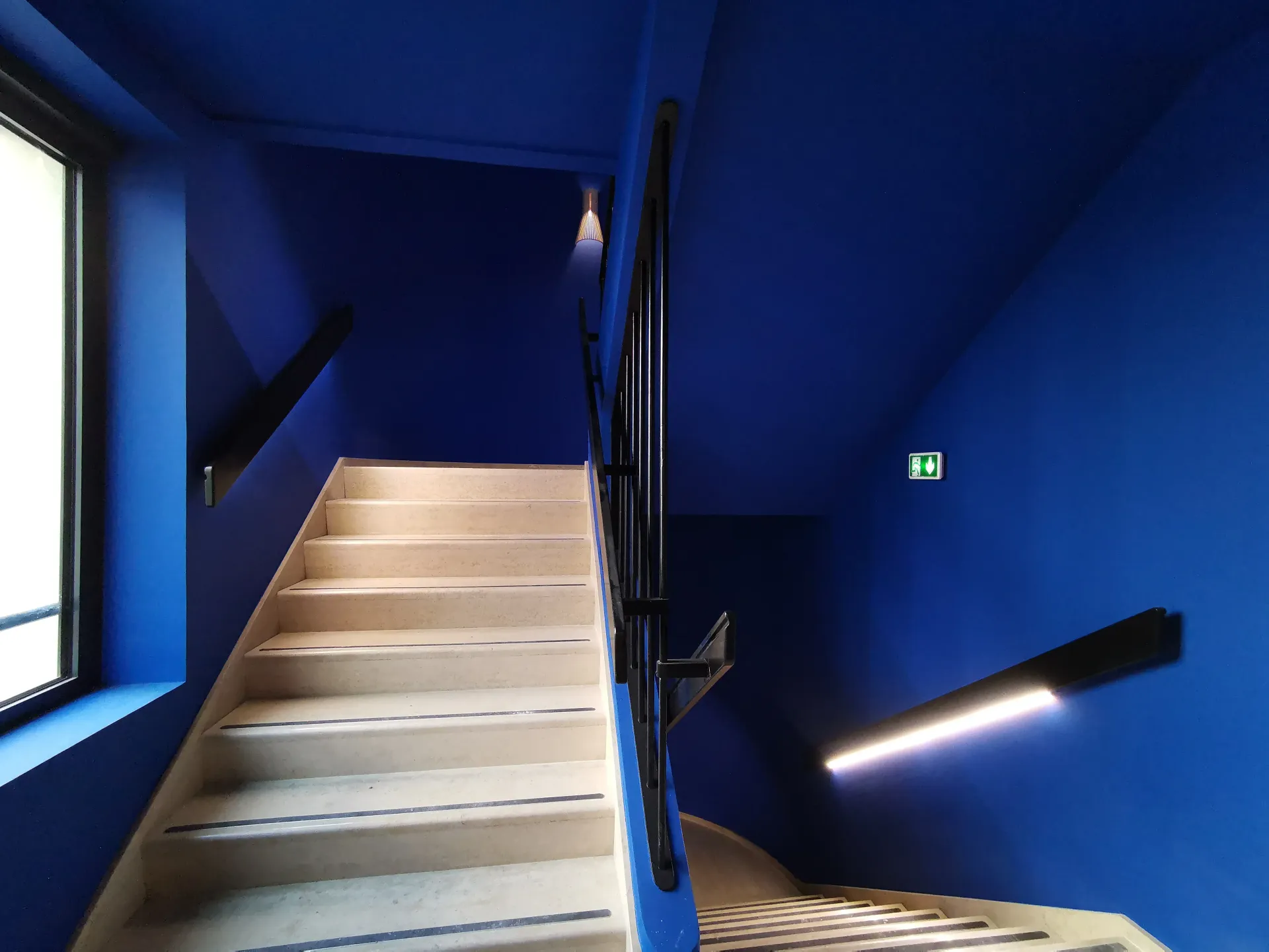 Un escalier avec des murs bleus et un panneau de sortie vert. Aménagement de bureaux et locaux professionnels - SPAC