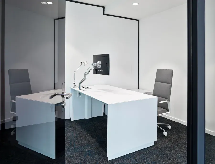 Un bureau blanc et une chaise dans un bureau avec un écran d'ordinateur sur le mur. SPAC