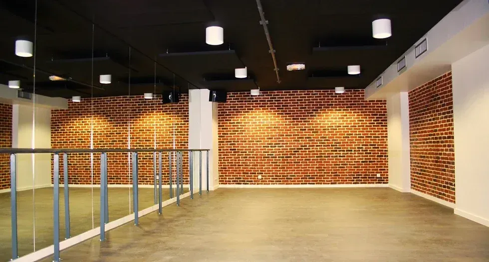 Une grande pièce vide avec un mur de briques et un miroir. Aménagement de bureaux et locaux professionnels - SPAC