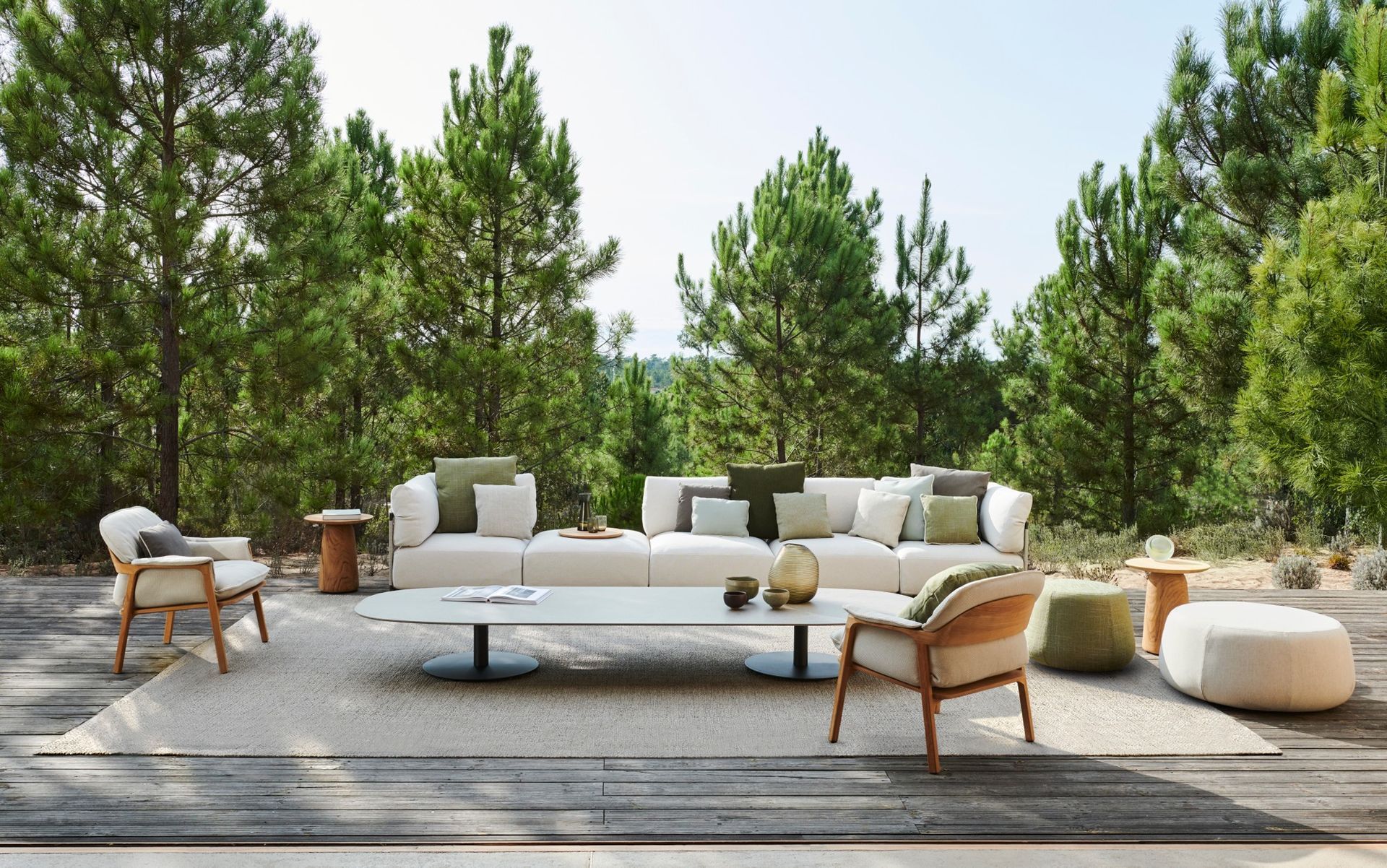 Een terras met een bank, stoelen, voetenbankjes en een tafel, omgeven door bomen.