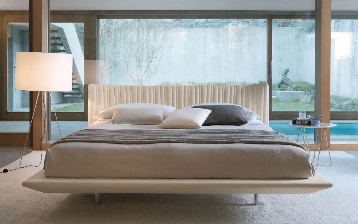 Een bed in een slaapkamer met een groot raam en een lamp.