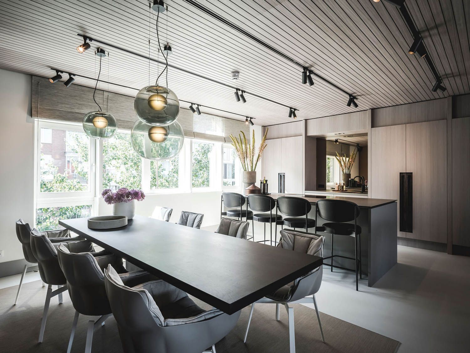 Een eetkamer met een lange tafel en stoelen en een keuken op de achtergrond.