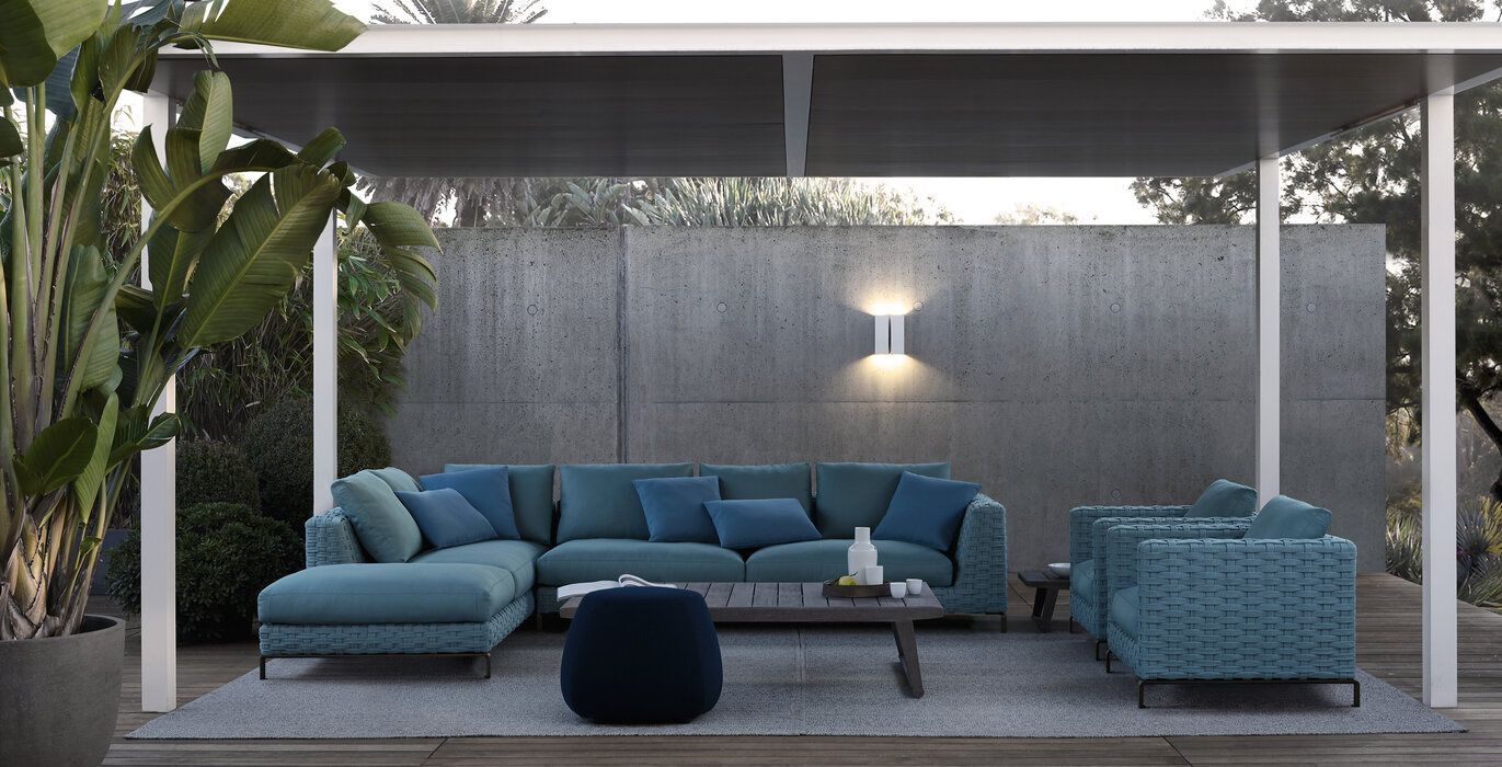 Een woonkamer met een blauwe hoekbank en stoelen onder een pergola.