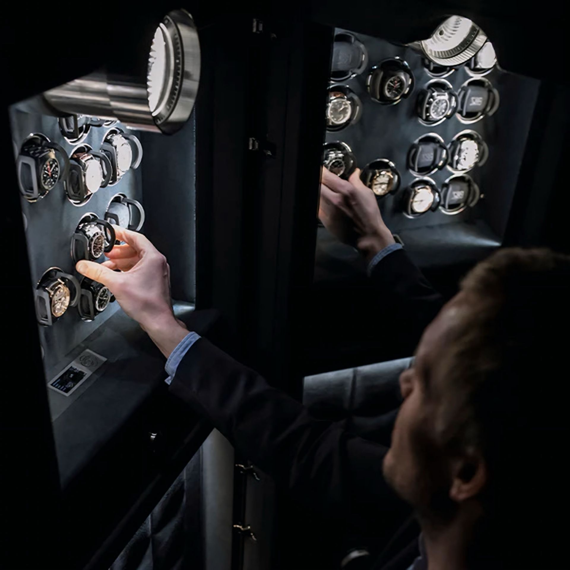 Een man in pak opent een kluis gevuld met horloges