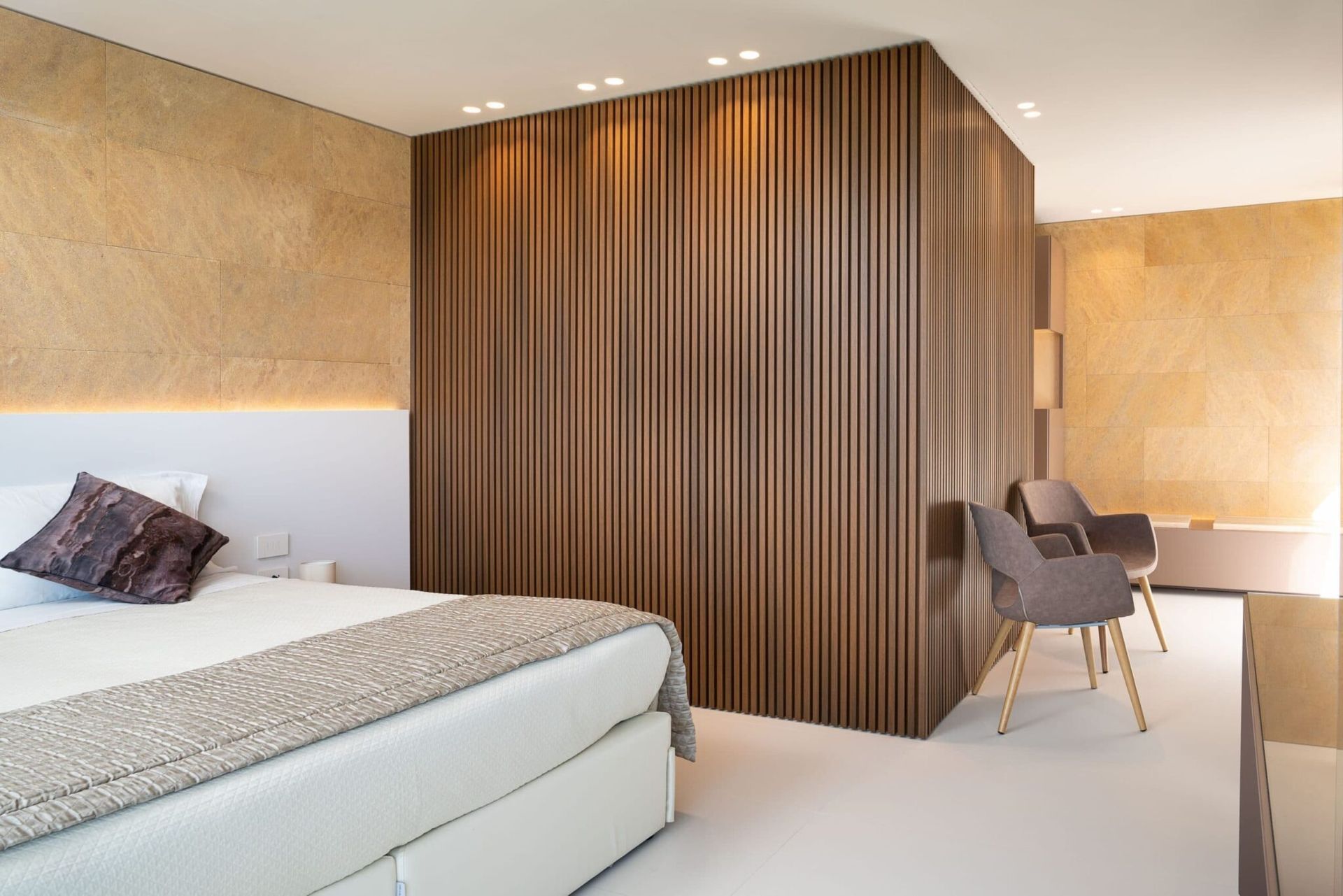 Een slaapkamer met een bed, stoelen en een houten muur.