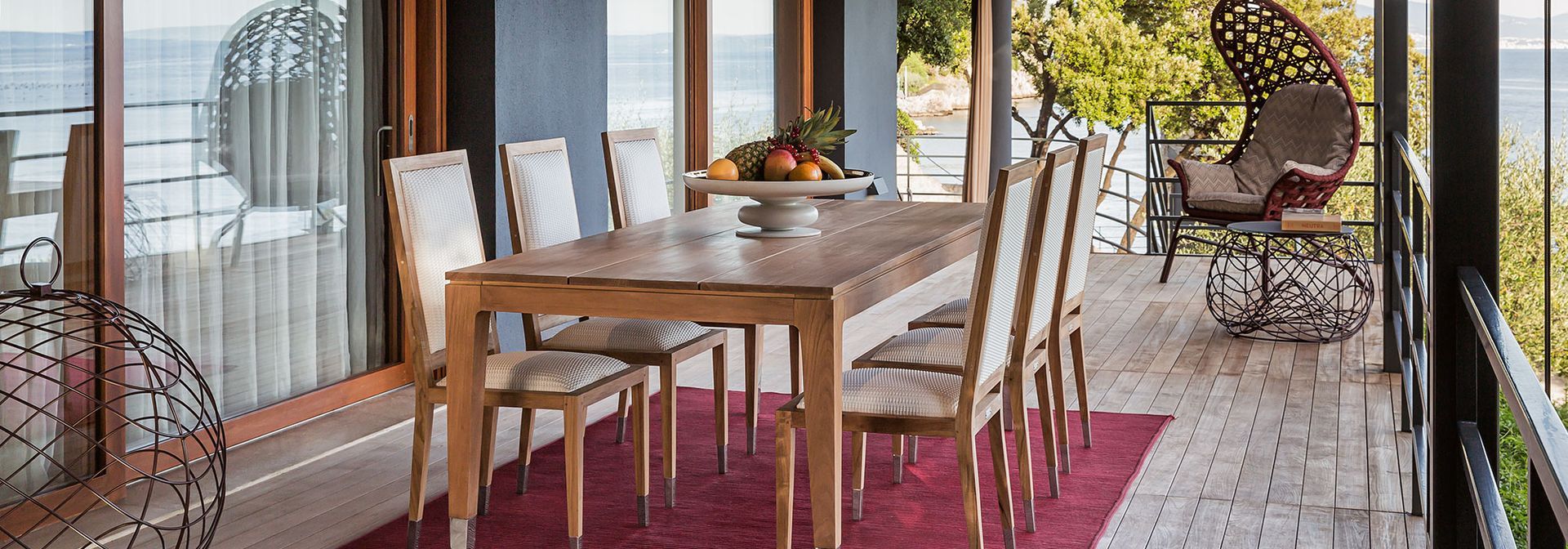 Een eetkamer met een tafel en stoelen op een balkon met uitzicht op de oceaan.