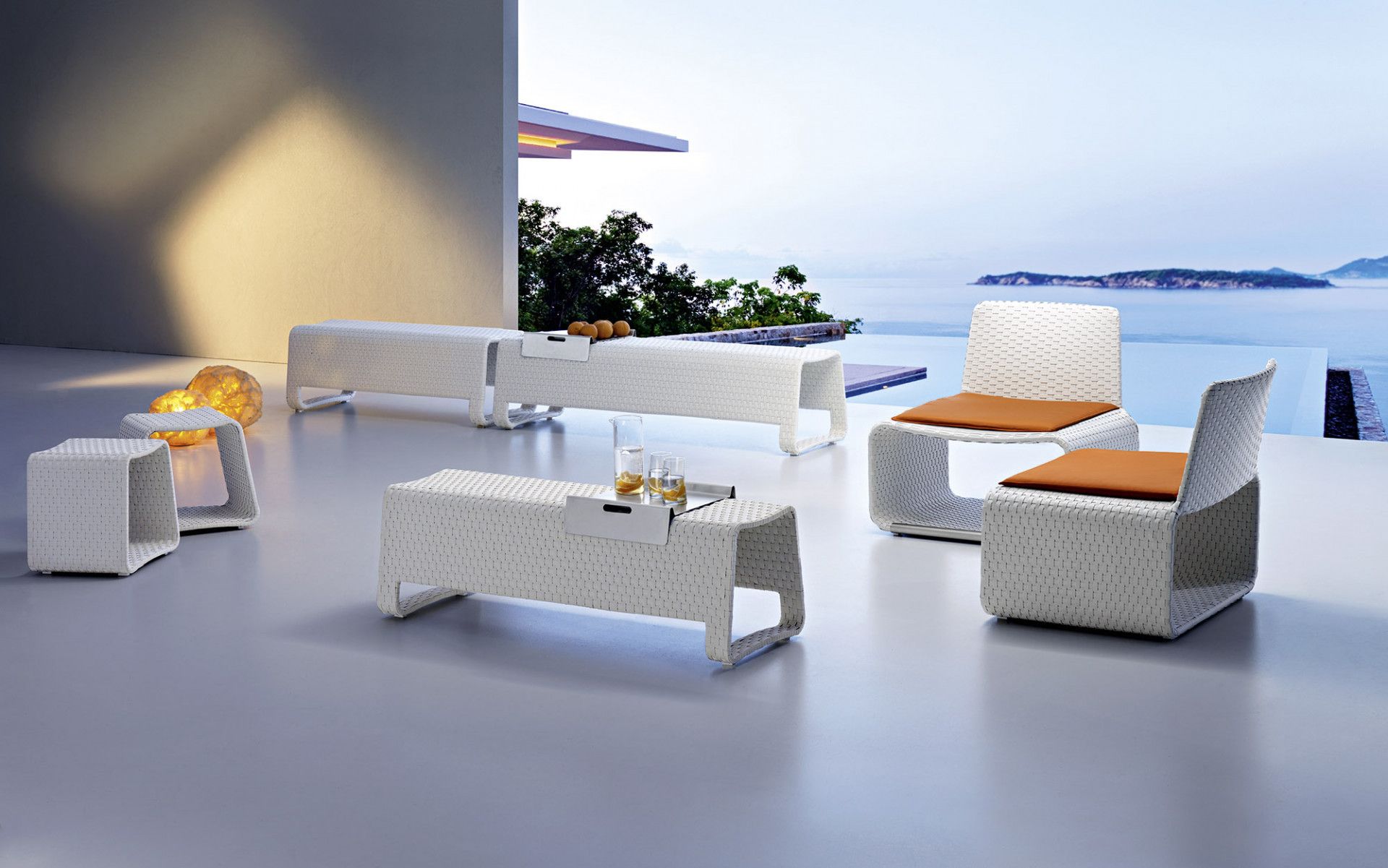 Een terras met een tafel, stoelen en voetenbankjes met uitzicht op de oceaan