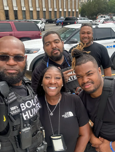 A group of people are posing for a picture in front of a police car.