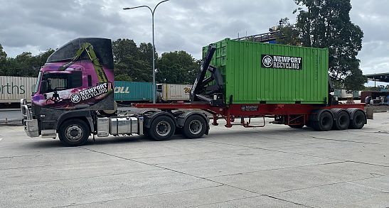 A Semi Truck is Carrying a Green Shipping Container on a Trailer — Newport Recycling in Woree, QLD