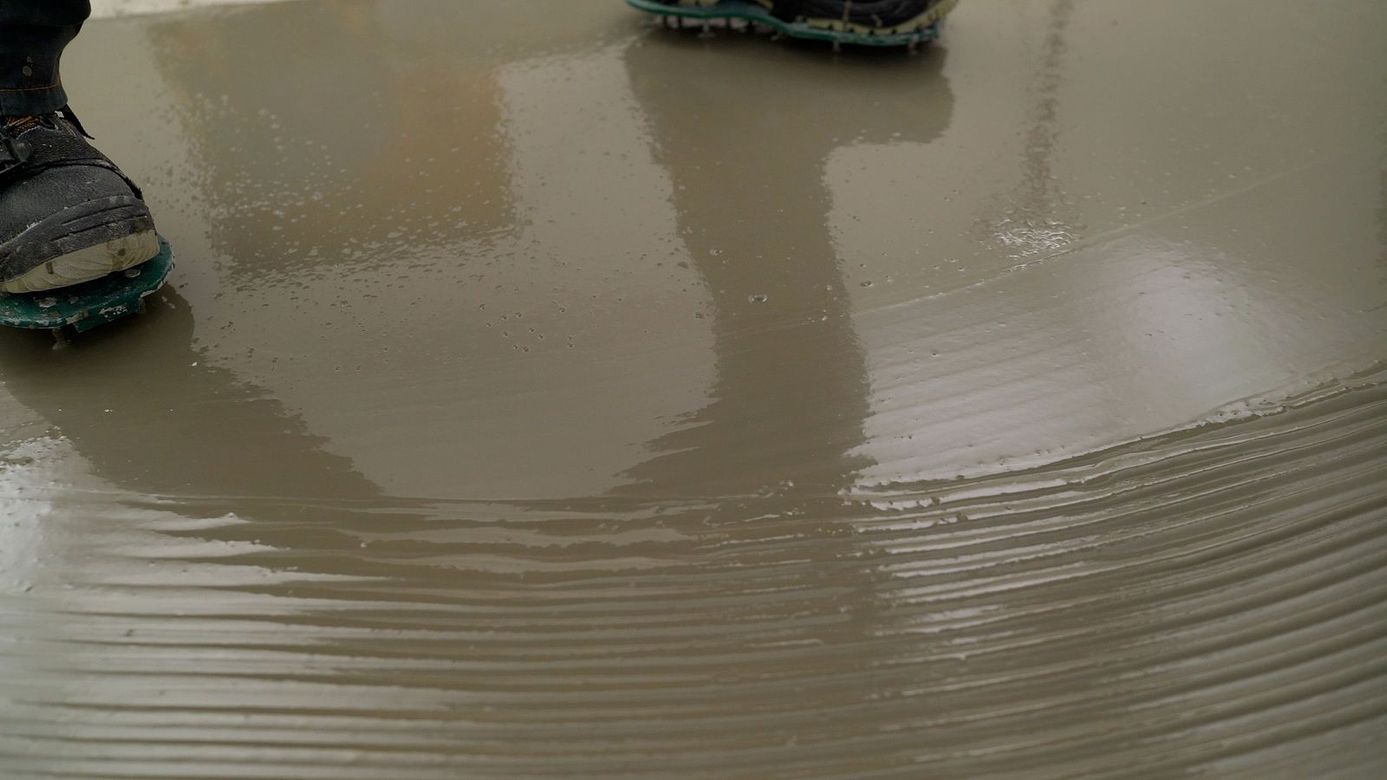 A person is spreading concrete on a wet floor.