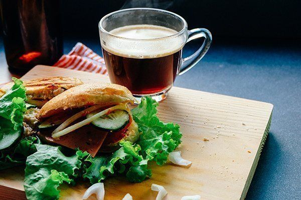 A sandwich and a cup of coffee on a wooden cutting board.