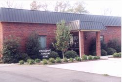 The Dyersburg Funeral Home building, a one-story brick structure with a dark metal roof and a small covered entrance.